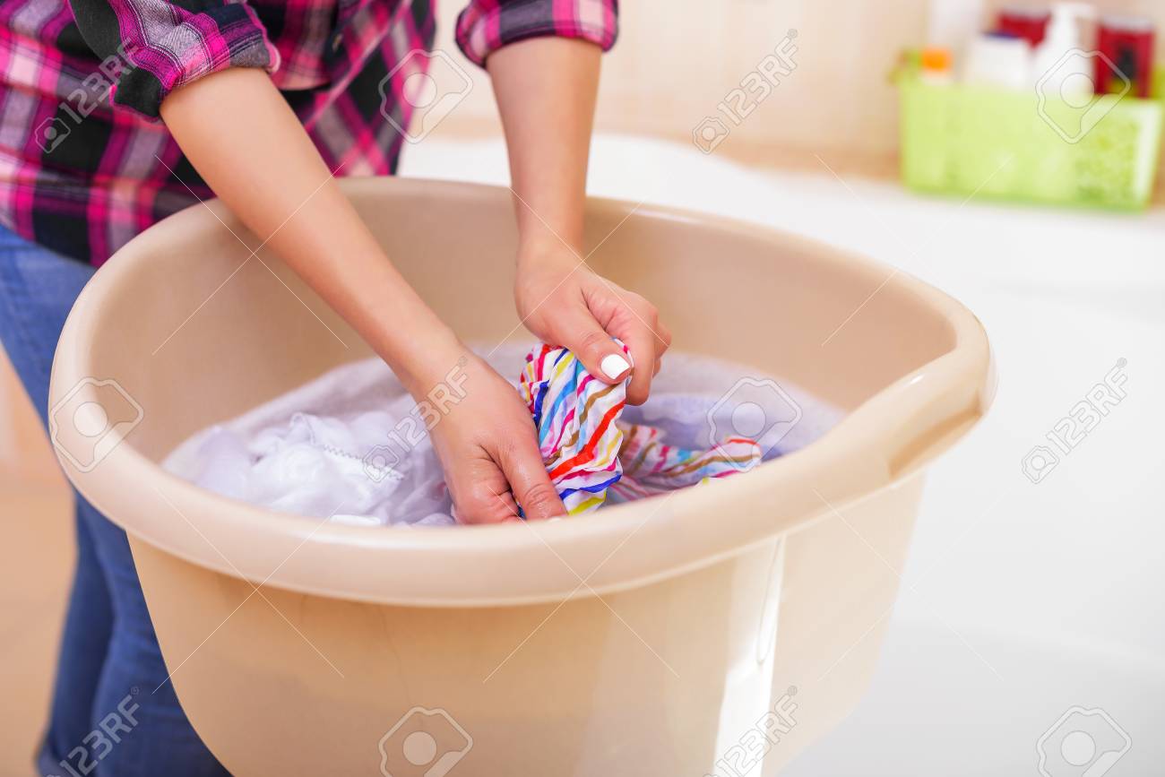 Women's hands wash clothes in the container. Close-up.