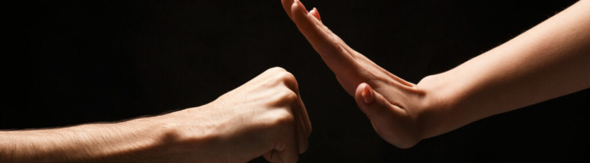 Male fist attacing and female hand in defense against black isolated backgorund. Stop violence against women concept, copy space